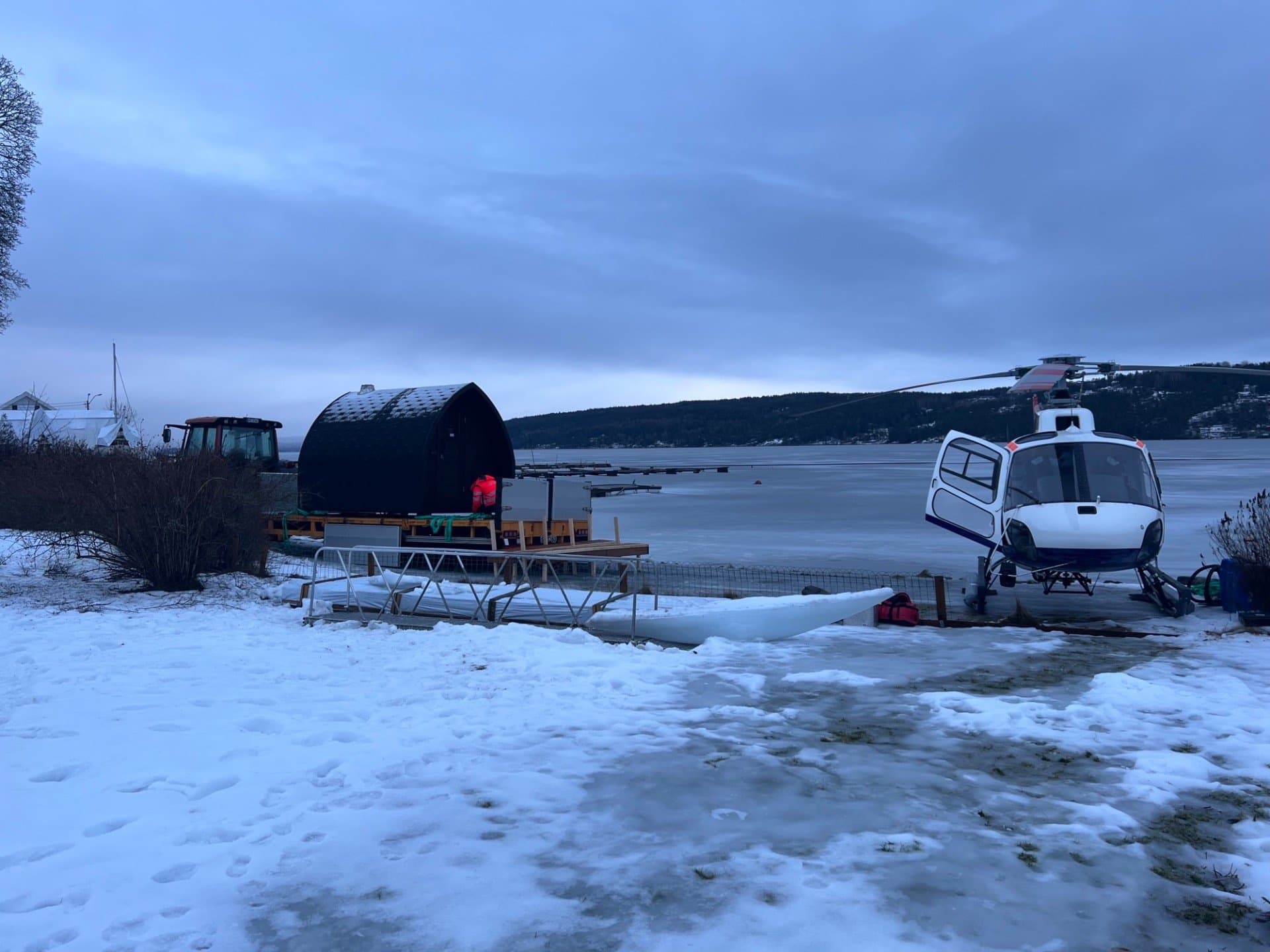 Mørk iglobadstue på en platting ved et islagt vann, med et landet helikopter ved siden av