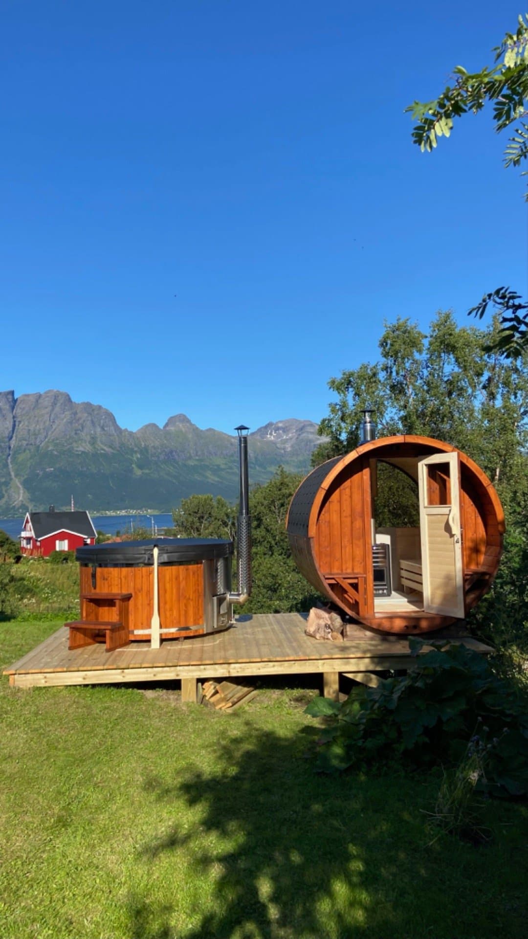 Tønnebadstue og badestamp på en treplatting, med fjord og fjell i bakgrunnen