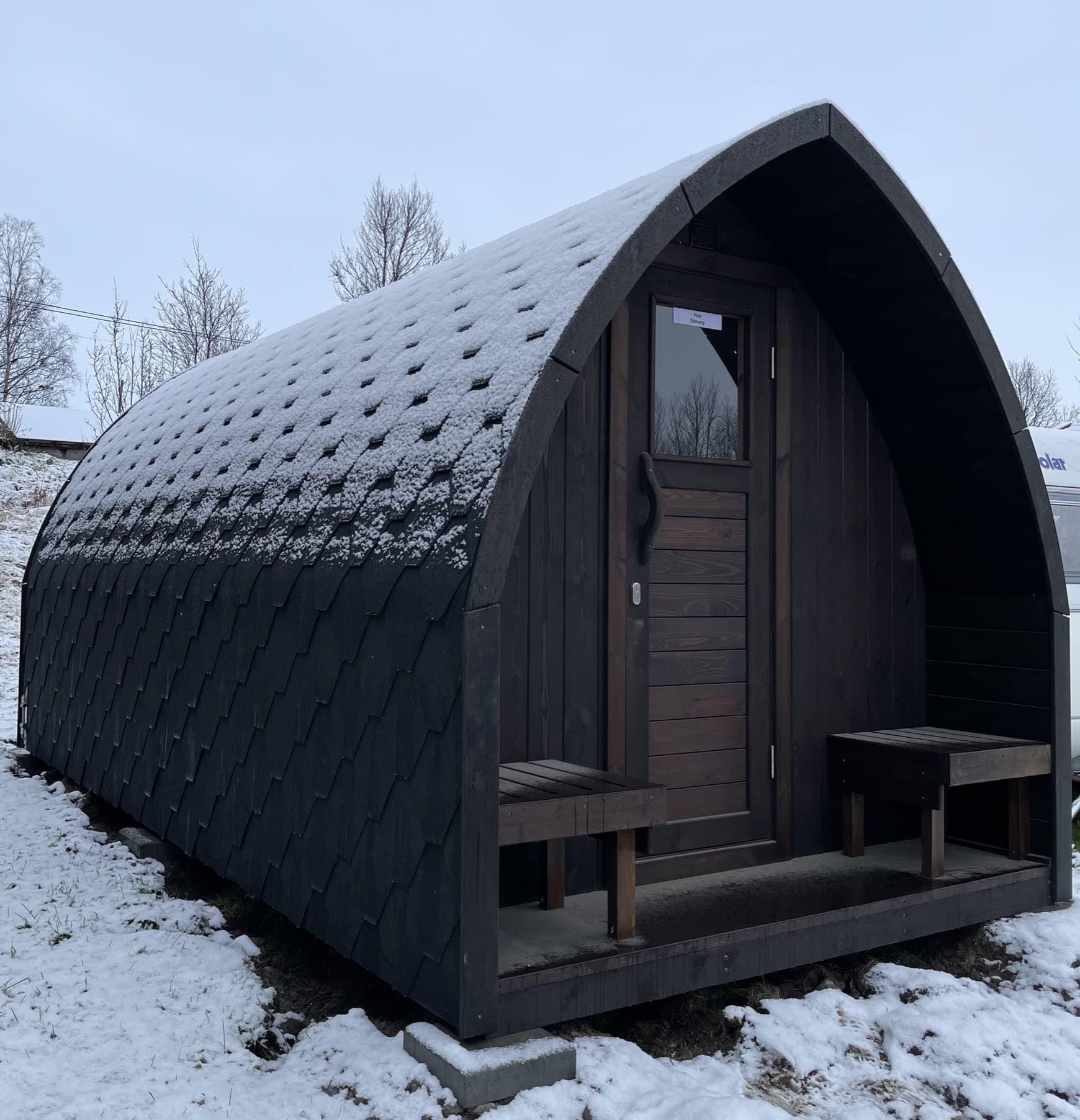 Mørk iglobadstue med takshingel og to benker ved døren, i snø