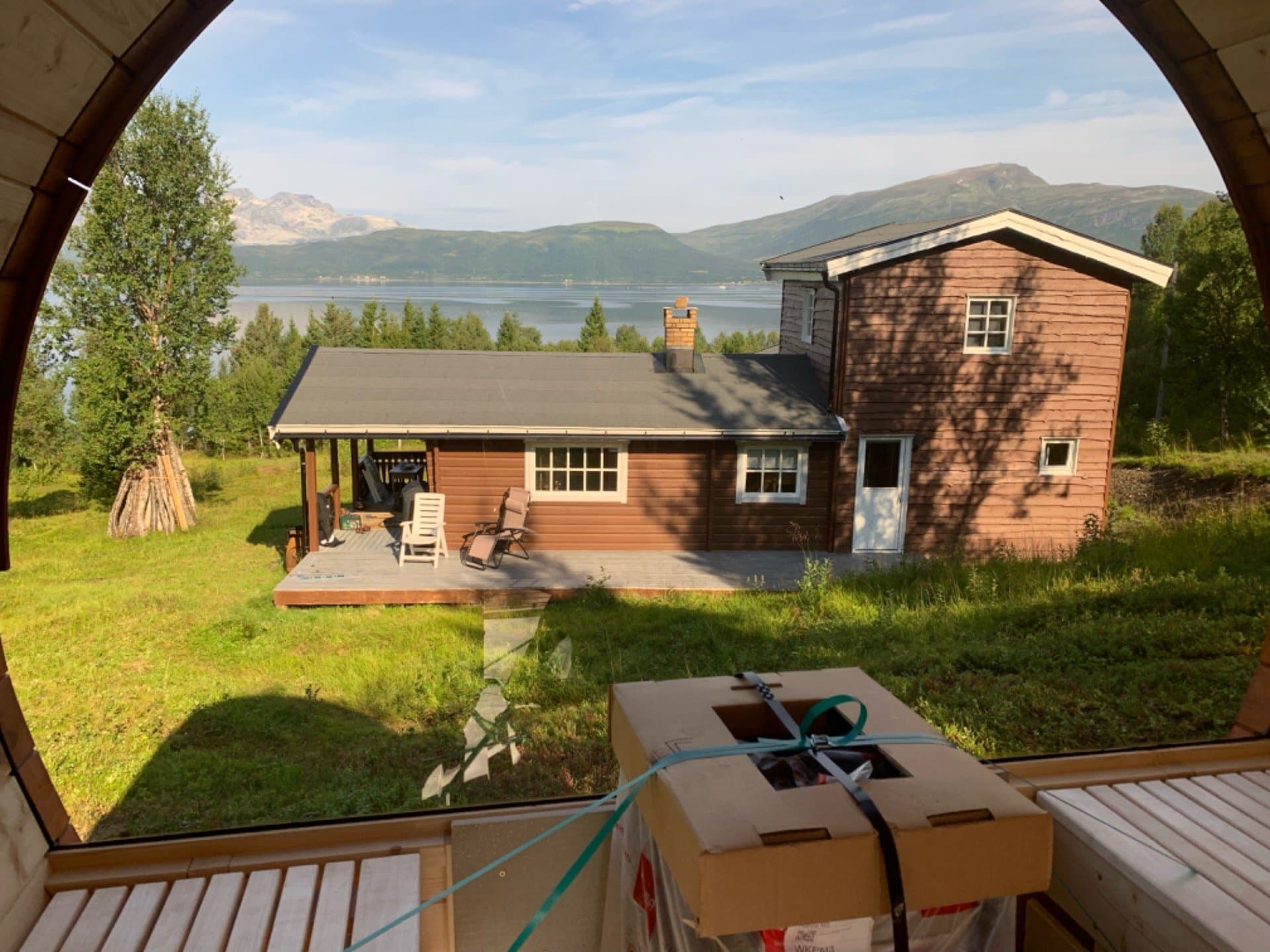 Utsikt gjennom det store panoramavinduet i tønnebadstuen mot huset og fjorden