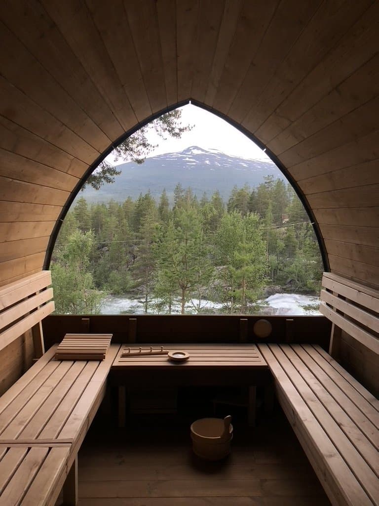 U-formet benk foran panoramavinduet i en iglobadstue, med utsikt mot skog og fjell