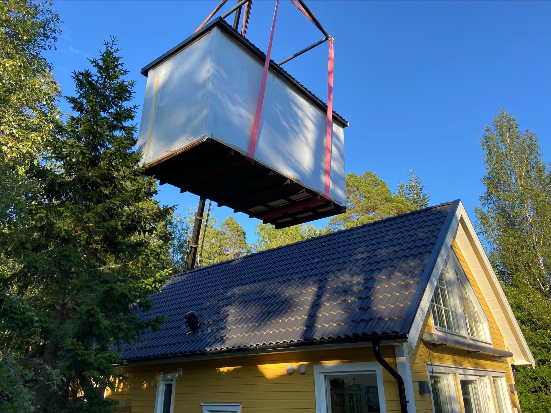 Innpakket badstue heises over taket på et gult hus