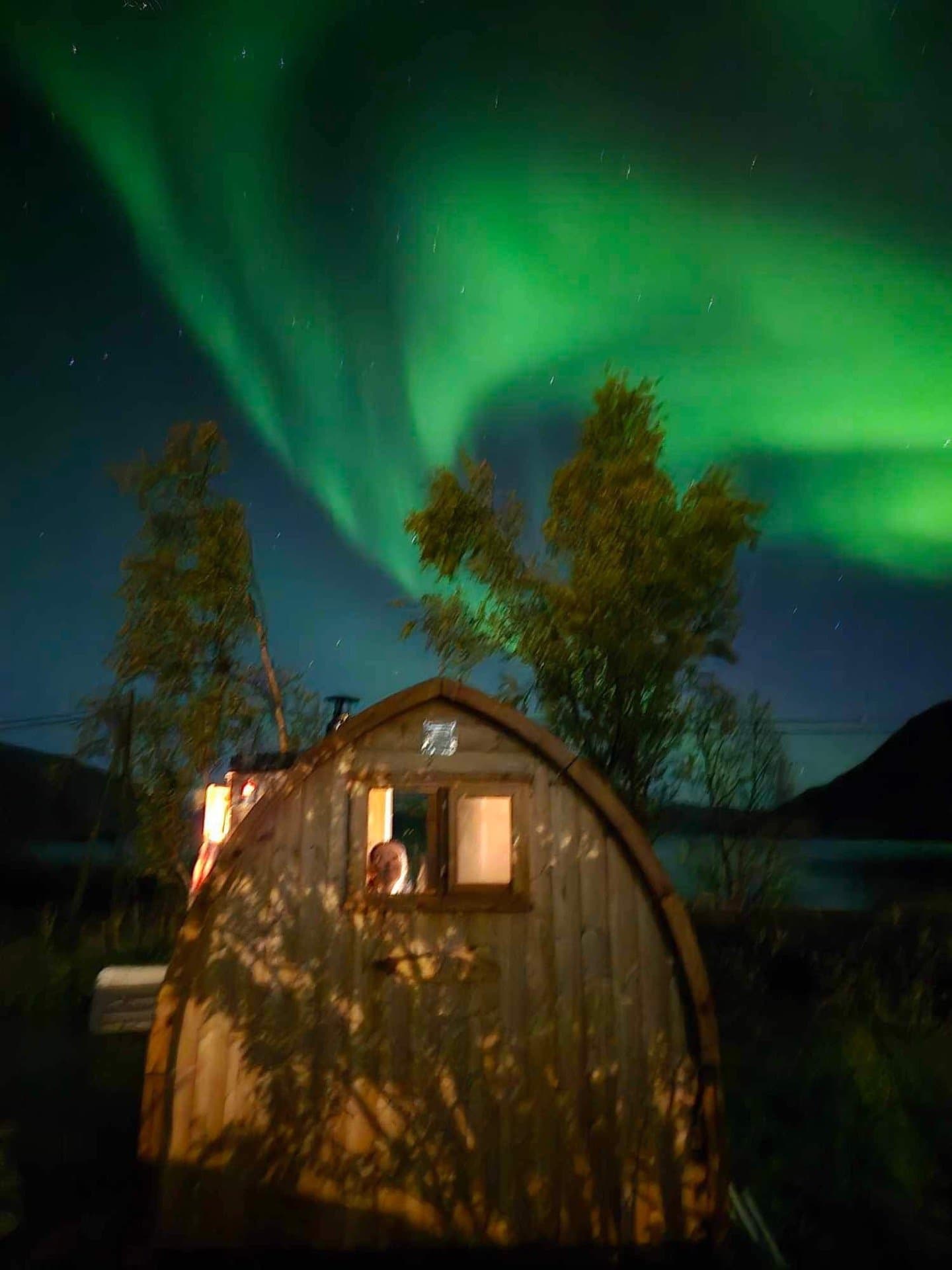 Iglobadstue med lys i vinduet under grønt nordlys