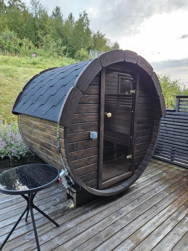 Liten mørk tønnebadstue med glassdør på en terrasse, med et glassbord ved siden av