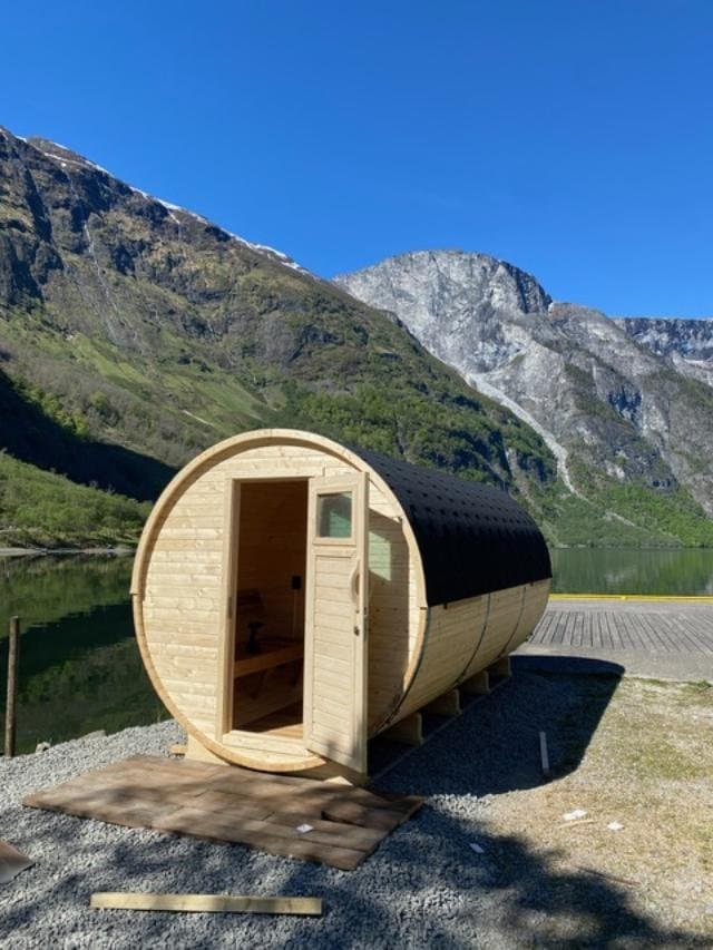 Tønnebadstue i ubehandlet tre ved en fjord med bratte fjell