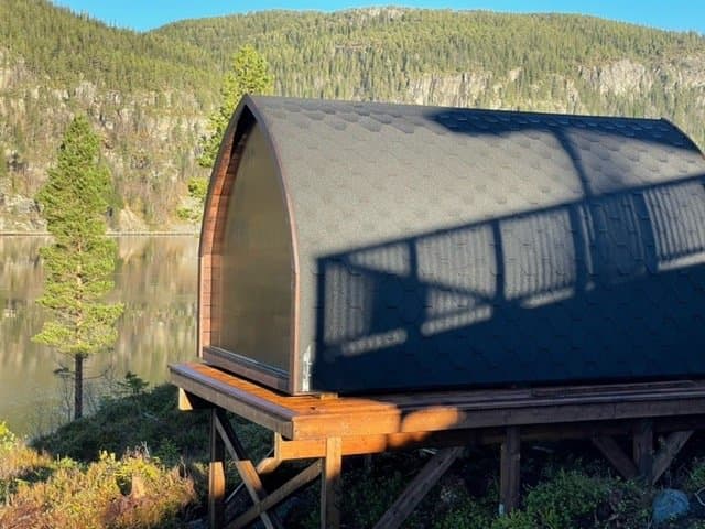 Iglobadstue på en hevet treplatting ved et vann, med skogkledde åser